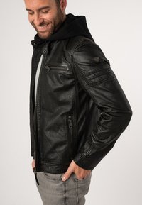 Schwarze Lederjacke mit durchgehendem Reißverschluss, Kapuzen-Design, gerippte Schulterakzente und mehreren Reißverschlusstaschen. Glatte Textur.