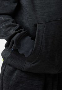 Zwarte sweatshirt van een getextureerde stof, met een voorzak, geribbelde manchetten en een bedrukt logo op de mouw. Accenten in verschillende kleuren.