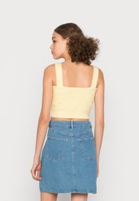 Top curto amarelo de malha com alças largas, combinado com uma saia A-line de ganga azul clara, com bolsos traseiros e uma cinta.
