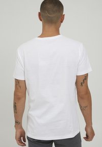 Hvit bomulls t-skjorte med korte ermer og rund hals. Bakvindu viser ingen grafikk eller mønstre; minimal tekstur.
