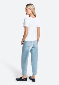 Haut blanc à manches courtes avec des bords scallopés, associé à un jean taille haute bleu clair et des mocassins noirs. Fond neutre.
