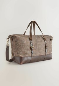 Brown leather bottom duffel bag with textured woven fabric body, dual handles, adjustable shoulder strap, and metallic buckles.