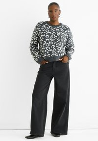 Gestrickter Pullover mit einem grau-weißen Leopardenmuster, rundem Ausschnitt und gerippten Bündchen. Kombiniert mit schwarzen weit geschnittenen Jeans.