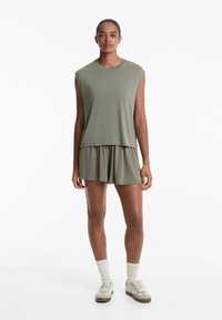Olivgrön ärmlös topp och matchande shorts i mjukt tyg. Avslappnad passform, lagerdesign med subtila fålldetaljer. Visade avslappnade skor.