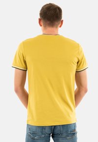 Camiseta amarilla de manga corta con cuello redondo, que presenta detalles a rayas en verde y blanco en las mangas. Tejido suave, corte casual.