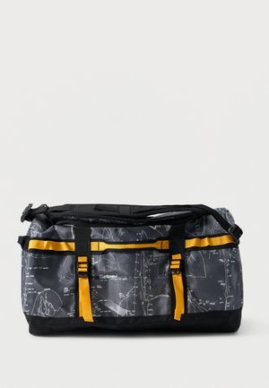 Čierno-sivá športová taška s bielymi mapovými vzormi, žltými remienkami, čiernymi prackami a nastaviteľným ramenným popruhom na jednoduchom pozadí.