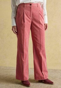 Velvetādas bikses maigi rozā krāsā ar priekšējiem krokām, platajiem bikšu galiem, jostasvietu ar pogas aizdari un teksturētu audumu.