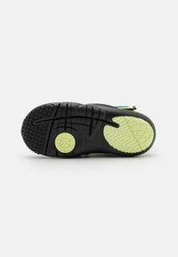 Black athletic shoe sole with a textured grip pattern, featuring a lime green accent and circular branding emblem.