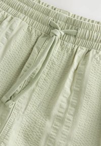 Pantalon en tissu vert clair texturé avec taille élastique et détail de cordon à nouer à l'avant.