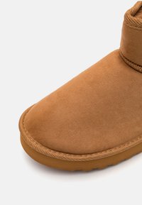 Bottine en daim tan avec un bout arrondi, semelle en caoutchouc plate et couture autour de la base. Texture douce et design minimaliste.