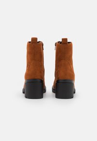 Hnědé semišové kotníkové boty s texturovaným povrchem, černým blokovým podpatkem a zipem vzadu. Jednoduchý design s poutkem na natažení.