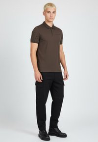 Brązowa koszulka polo o slim fit, z krótkimi rękawami i zapięciem na guziki, zestawiona z czarnymi spodniami cargo i czarnymi sznurowanymi butami.