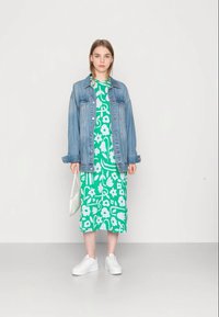 Vestido midi com padrão floral verde, combinado com uma jaqueta de ganga azul clara e sapatilhas brancas. O vestido apresenta flores de grandes dimensões e um tecido suave.