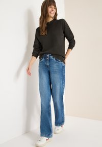 Ciemny, prążkowany sweter w połączeniu ze światłymi, szerokimi dżinsami. Dopełnieniem codziennego looku są sneakersy z beżowymi podeszwami i czerwonymi akcentami.