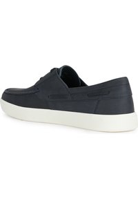 Zapato de piel azul marino sin cordones, de perfil bajo y suela de goma blanca. Presenta costuras sutiles y cortes laterales para una mejor transpirabilidad.