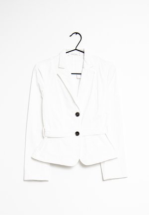 Witte getailleerde blazer met twee zwarte knopen, ingesneden revers en peplumzoom hangend aan een zwarte hanger tegen een witte achtergrond.