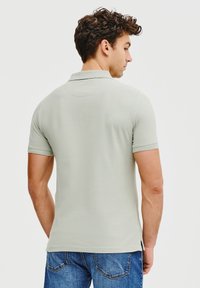 Jasnozielona, krótko rękawowa koszulka polo z klasycznym kołnierzykiem i bocznymi rozcięciami. Gładka faktura materiału. Nosi się z niebieskimi dżinsami.