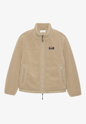 Beige fleece jacket with a high collar, front zipper, two side pockets, and a chest patch featuring the brand name. Soft, textured fabric.