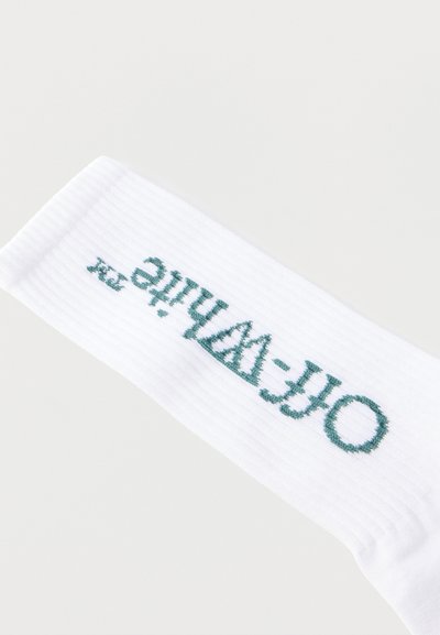 Άσπρη ριγέ κάλτσα με κεντητό κείμενο σε τυρκουάζ χρώμα που γράφει "OFF-WHITE", τοποθετημένο διαγώνια σε ένα απλό ανοιχτόχρωμο φόντο.