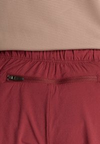 Pantaloncini color mogano con superficie strutturata, vita elastica e una tasca con cerniera sul retro. Il materiale sembra leggero e traspirante.