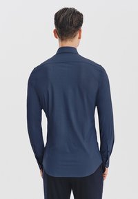 Granatowa koszula z długim rękawem, wykonana z teksturowanej tkaniny, z klasycznym kołnierzykiem i zapięciem na guziki przy mankietach, o dopasowanym kroju i zaokrąglonym dole.