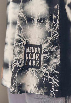 Schwarz-weißes Grafik-T-Shirt mit einem Blitzmuster und dem Text "NIE ZURÜCKSCHAUEN" in einer fetten, dunklen Schrift auf einem strukturierten Stoff.