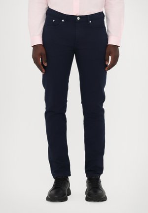 Marineblauwe katoenen jeans met een slim fit, voorzien van vijf zakken, een metalen knoop en een ritssluiting. Zwarte sportschoenen maken de look compleet.