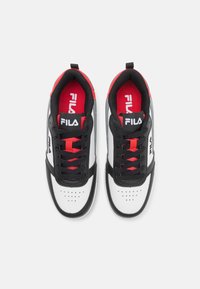 Zapatillas deportivas blancas con acentos negros y detalles rojos. Cuentan con una superficie texturizada, perforaciones, cordones negros y un logo en la lengüeta.
