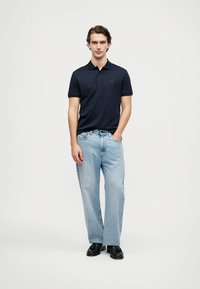 Námořnická polo košile s krátkým rukávem a límečkem, zkombinovaná se světle modrými rovnými džíny a černými botami. Jednoduchý, ležérní styl.