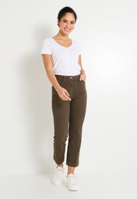 Pantalon vert olive foncé avec taille haute et coupe slim. Associé à un t-shirt blanc à col en V et des baskets blanches. Design simple sans motifs.