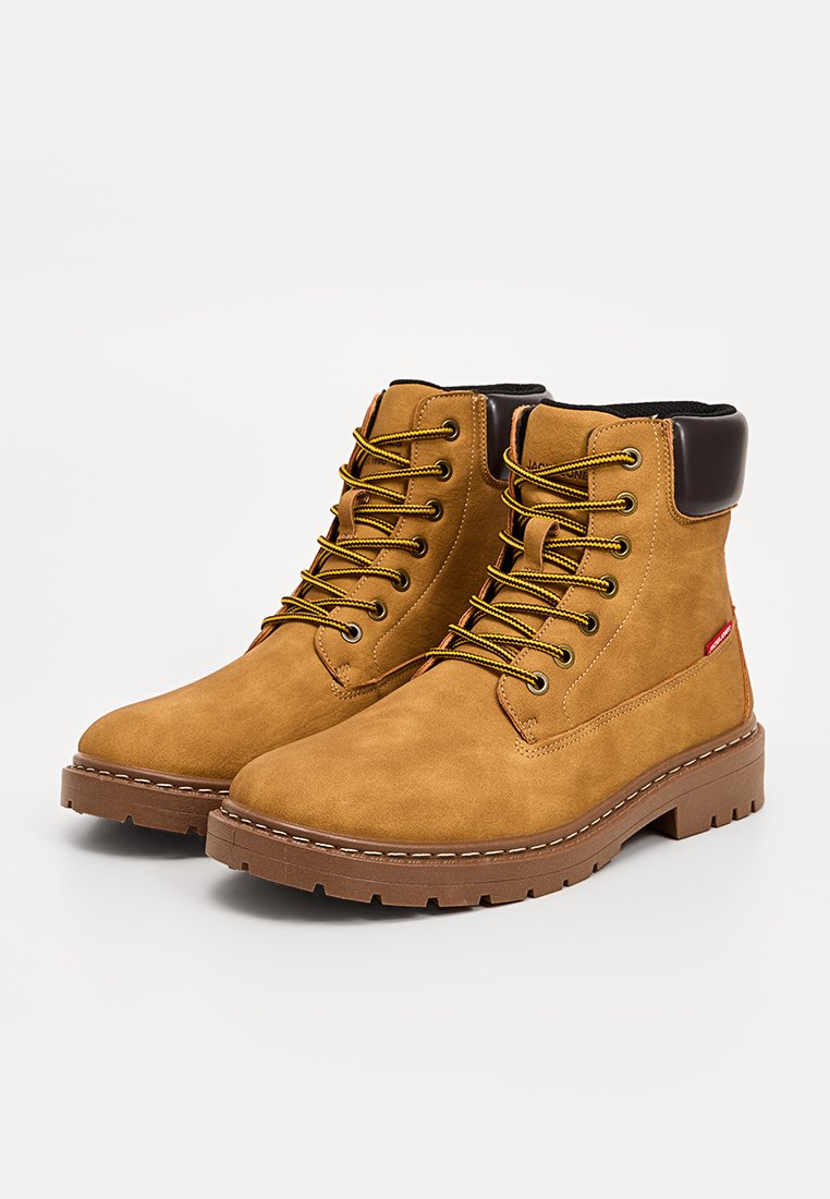 Stivaletti alla caviglia in camoscio tan con suole in gomma marrone, parte superiore testurizzata, lacci gialli e bordino alla caviglia in pelle marrone a contrasto.