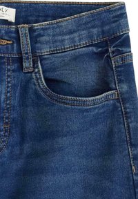 Modré džíny z denimu s polovičním pasem, klasickým designem pěti kapes, viditelným šitím a vybledlou texturou na vybraných místech.