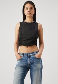 Svart cropped topp med rynkedetaljer, uten ermer, kombinert med lyseblå denimjeans med avslappet passform og falmet tekstur.