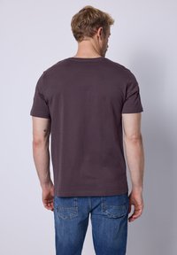 Camiseta gris de manga corta hecha de algodón, con cuello redondo y un ajuste relajado. Combinada con jeans de mezclilla azul, mostrando un diseño sencillo.