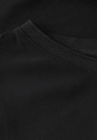 Tissu noir avec une texture douce et un col à bande plate. Le matériau semble lisse et légèrement extensible. Détails de couture minimaux visibles.
