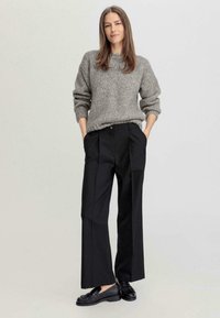 Suéter gris de punto con un corte holgado y puños acanalados, combinado con pantalones negros de cintura alta con pliegues, usados con zapatos negros.