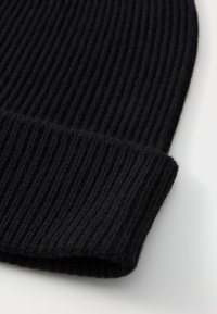 Black knit beanie with ribbed texture. Features a folded cuff, made of soft fabric, showcasing a close-up of its detailed knit pattern.