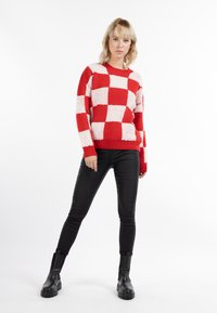 Suéter a rayas rojas y blancas con una superficie texturizada, cuello redondo y puños acanalados, combinado con jeans skinny negros y botas negras hasta el tobillo.