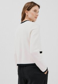 Maglione bianco con bordi neri, scollatura rotonda e vestibilità su misura. Un dettaglio notevole è l'accento nero al polsino e la texture liscia.