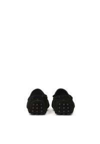 Mocasines de ante negro con punta redonda, diseño sin cordones y suelas de goma texturizadas que presentan patrones circulares elevados en el talón.