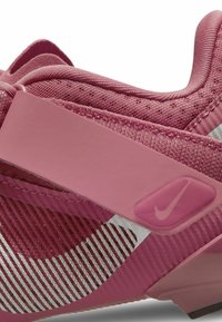Růžová atletická bota z prodyšných a syntetických materiálů, s texturovaným svrškem, bílými akcenty a výrazným logem Nike na boku.