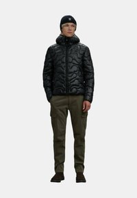 Giacca nera imbottita con colletto alto, caratterizzata da un motivo trapuntato. Abbinata a pantaloni cargo olive e un berretto di maglia blu navy. Calzature marroni.