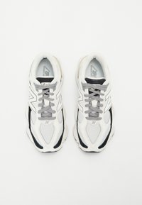 White mesh and synthetic sneakers with black accents, grey laces, and textured soles featuring a prominent logo on the side.