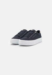 Pár námořnických modrých plátěných tenisek s bílými silnými podrážkami, tkaničkami a logem Tommy Hilfiger na boku a patě.