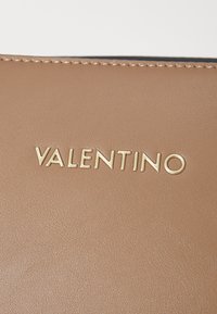 Pelle texturizzata di colore marrone chiaro con logo "VALENTINO" dorato. Finitura liscia, dettagli di cucitura minimali. Design compatto per una facile maneggevolezza.