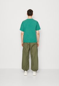 Tyrkysové tričko s kulatým výstřihem, spárované s volnými olivově zelenými cargo kalhotami. Model nosí bílé tenisky.