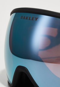 Lunettes Oakley avec un objectif miroir teinté de bleu et une monture noir mat. Rembourrage noir texturé visible sur le côté intérieur.