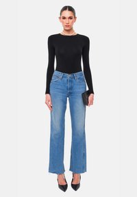 Zwarte lange mouwen bodysuit, hoog-getailleerde lichtblauwe flared jeans met raw hem, gecombineerd met zwarte puntige hakken, terwijl een zwarte clutch wordt vastgehouden.