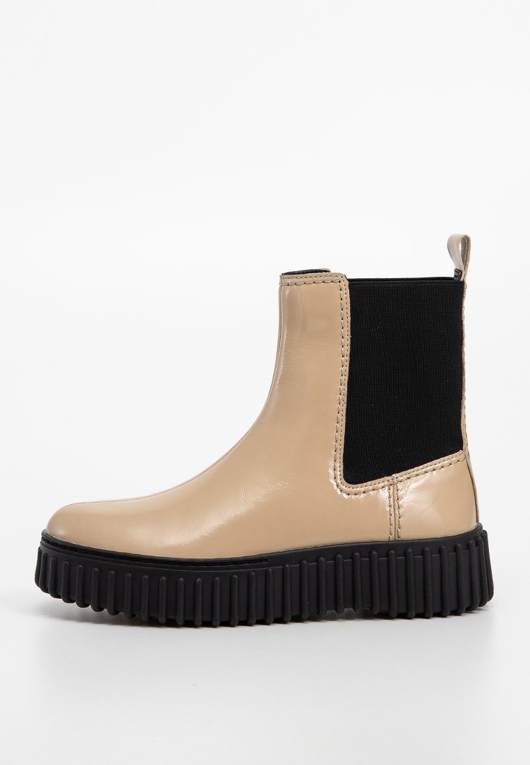 Stivale alla caviglia in pelle beige con pannelli elastici neri, punta arrotondata e una suola nera spessa e scanalata per una maggiore aderenza e stabilità.