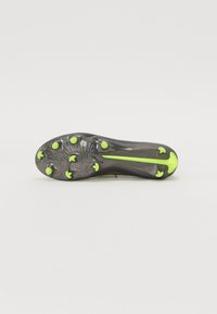 Suela de tacón negra de botas de fútbol con una superficie texturizada, que presenta tacos verdes y un diseño central. Los acentos incluyen una franja con un logo prominente.